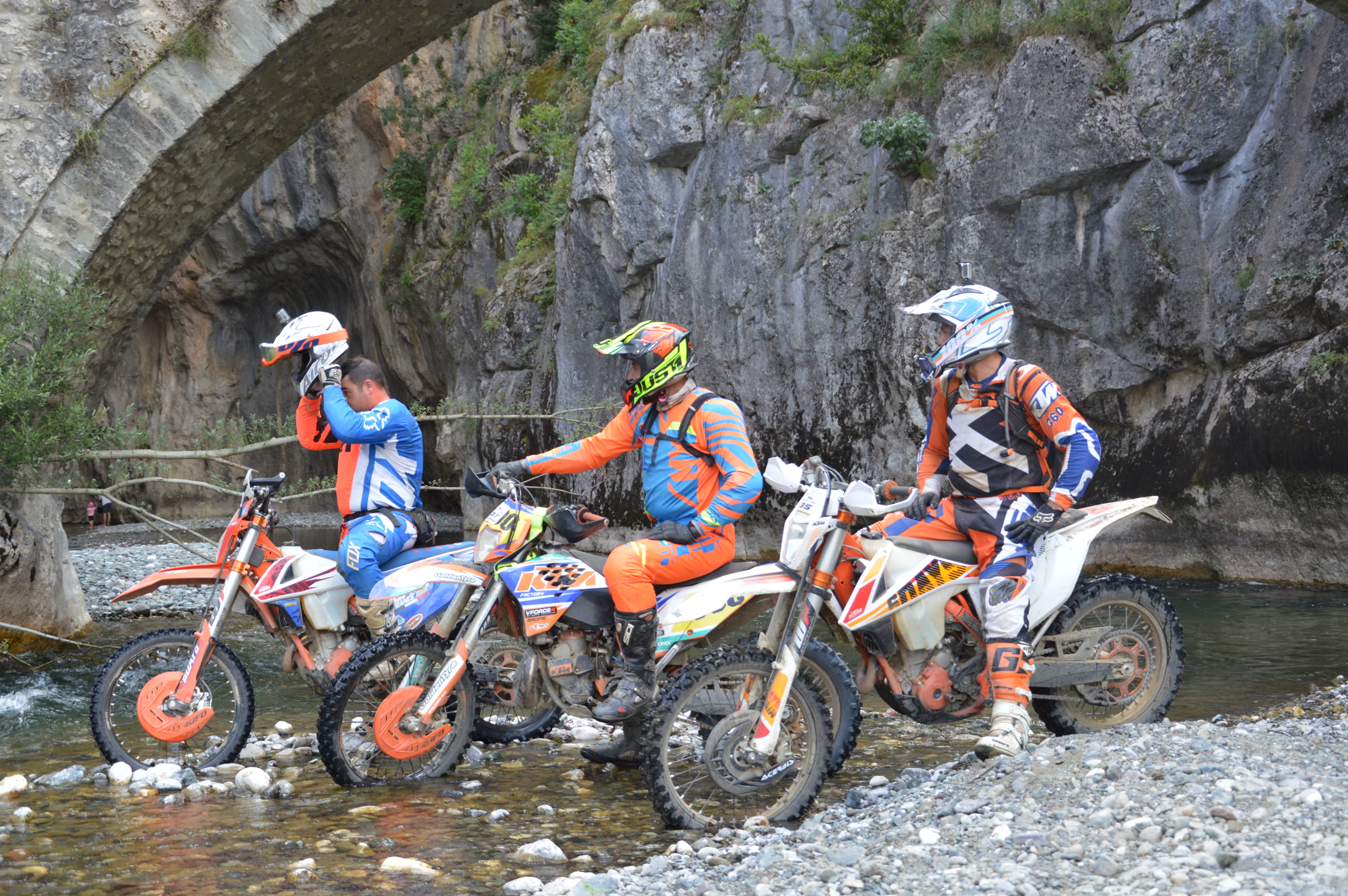 Three enduro riders assembled in the river beneath the bridge