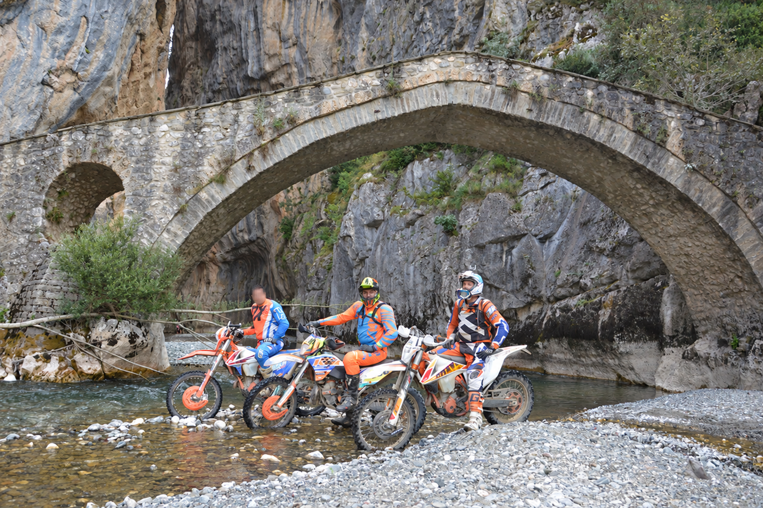 Enduro riders beneath the landmark stone bridge in Grevena